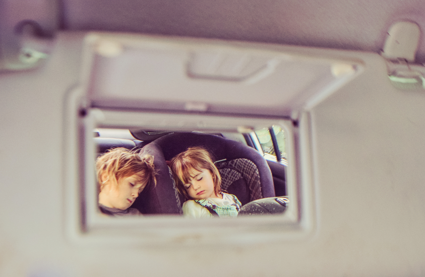 Two kids asleep in the backseat, seen from the rearview vanity mirror